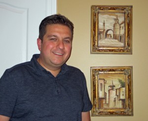 Dr. Omar Salem stands next to images of old Syria in the foyer of his home.