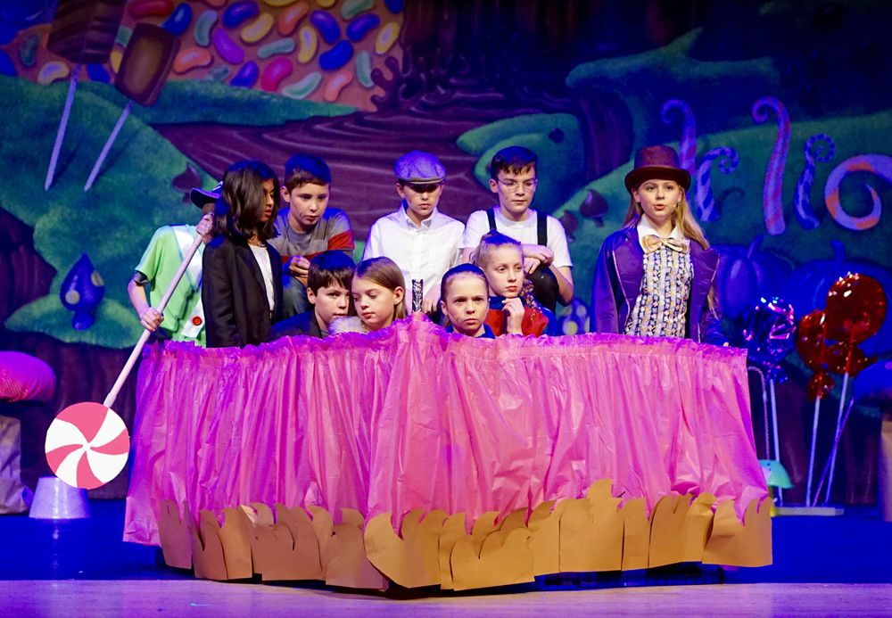 (Front row) Aiden Canny as Mr. Salt, Kayleigh Brown as Veruca Salt, Jessica Hooton as Violet Beauregarde, Gabrielle Conard as Mrs. Beauregarde, Anna Persson as Willy Wonka; (back row) Nishka Baduamanda as Mrs. Teavee, Aidan O’Toole as Mike Teavee, Abby Porter as Charlie Bucket, and Sean Keevan as Grandpa Joe